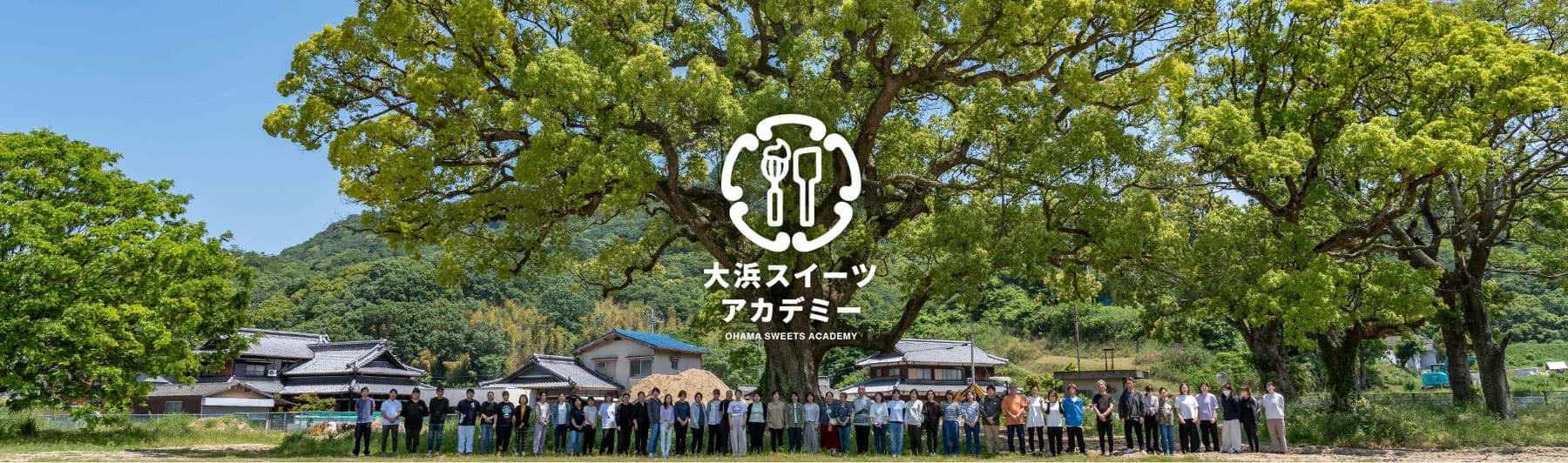 大楠の前に集まる大浜スイーツアカデミーの人々と校舎の風景